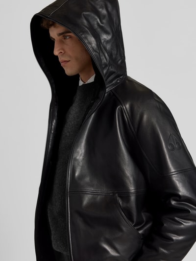 Männermodel trägt Jacke in Leder-Optik von Moose Knuckles, Schwarz, Zweiwege-Reißverschluss, Känguru-Tasche, Nahaufnahme Oberkörper.