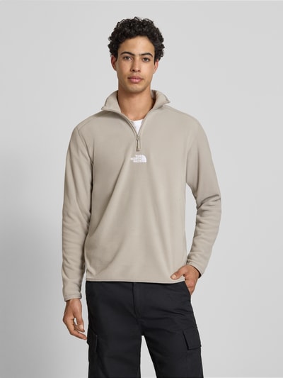 Męski model nosi Fleecepullover mit Reißverschluss Modell 'GLACIER' von The North Face, krój regular fit, stójka, wyhaftowane logo, zamek błyskawiczny, długość tyłu 70 cm, długość rękawów 67 cm, jasny beż, gładka faktura, Ganzkörperansicht von vorne.