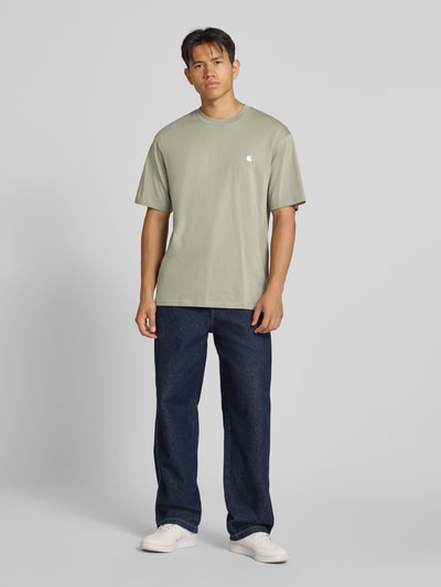 Männermodel trägt Regular Fit T-Shirt aus reiner Baumwolle Modell 'Madison' von Carhartt Work In Progress, dezentes Grün, Ganzkörperansicht von vorne. Herren T-Shirt mit Rundhalsausschnitt, Label-Stitching, Rückenlänge bei Größe M 78 cm, glatte Struktur.