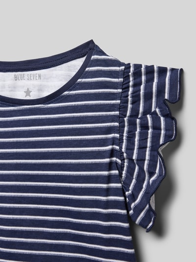 Mädchen trägt Regular Fit T-Shirt mit Rüschenbesatz von Blue Seven, gestreift in Blau-Weiß, Reine Baumwolle, Brusttasche, Nahaufnahme Oberkörper.