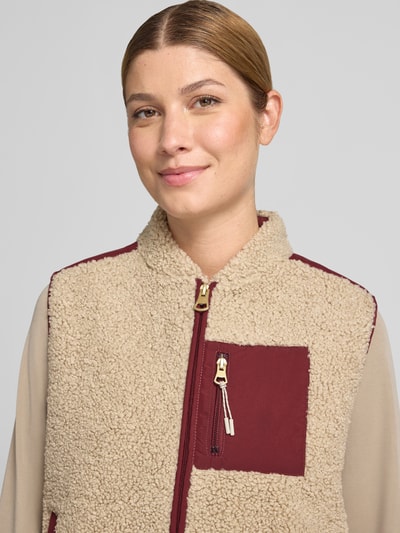 Frauenmodel trägt Weste mit Zweiwege-Reißverschluss und Brusttasche Modell 'Rowe' von MOS MOSH aus beigefarbenem Teddyfell mit weinroten Akzenten, Regular Fit, Nahaufnahme Oberkörper.