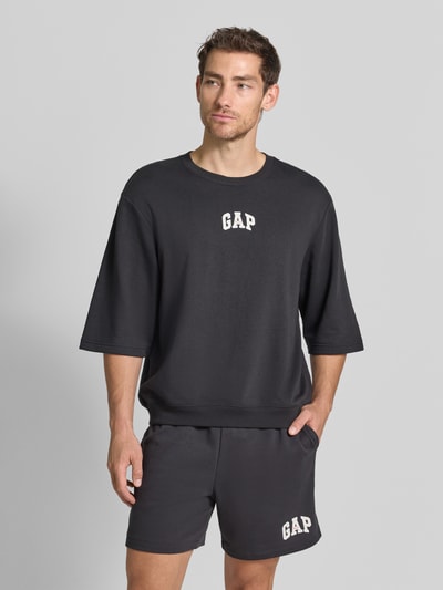 Männermodel trägt T-Shirt mit Rundhalsausschnitt und Logo-Print von GAP aus katoenmix, loose fit, ribboorden, logoprint, zwarte kleur, ruglengte bij maat M 70 cm, Ganzkörperansicht van voren