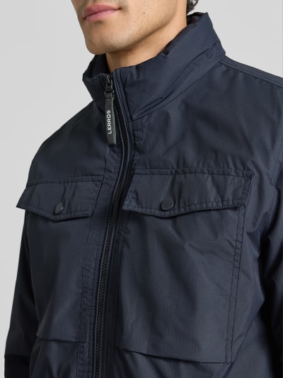 Mannenmodel draagt Jacke mit Stehkragen und Reißverschlusstaschen van LERROS in donkerblauw met opstaande kraag, rits, borstzakken, regular fit, detailopname bovenlichaam, ruglengte maat M 60 cm, schouderbreedte 48 cm, borstwijdte 58 cm, mouwlengte 60 cm.