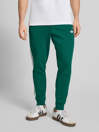 Männermodel trägt Sweatpants mit elastischem Bund von adidas Originals in Dunkelgrün, Baumwoll-Elasthan-Mix, lockerer Schnitt, Nahaufnahme Unterkörper.
