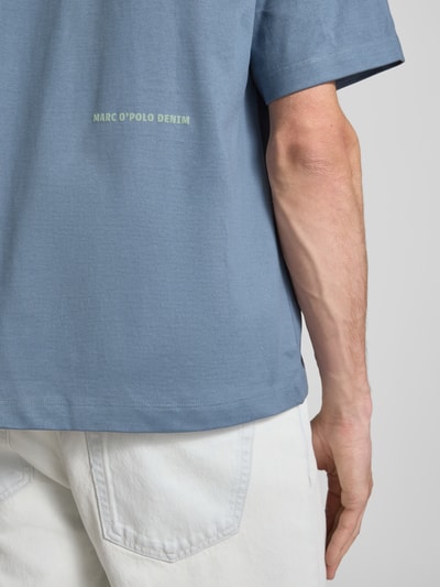 Männermodel trägt Boxy Fit T-Shirt aus reiner Baumwolle von Marc O'Polo Denim in Blau mit Label Print, unifarben, Detailaufnahme Rücken.