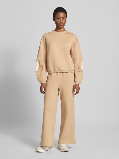 Frauenmodel trägt Wide Fit Sweatpants aus Baumwoll-Mix Modell 'Gunda' von GUIDO MARIA KRETSCHMER WOMAN in Beige, mit Logo-Print und elastischem Bund, Eingrifftaschen, Ganzkörperansicht von vorne.