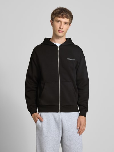 Männermodel trägt Relaxed Fit Sweatjacke aus Baumwoll-Mix mit Label-Detail von REVIEW in Schwarz, geteilte Känguru-Tasche, Ganzkörperansicht von vorne.