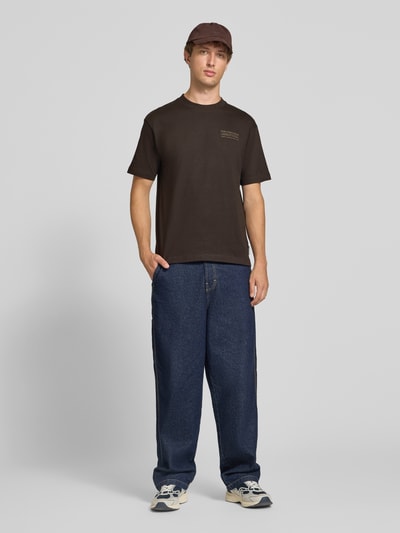Männermodel trägt Relaxed Fit T-Shirt aus reiner Baumwolle von Marc O'Polo, dunkelbraun, weite Passform, kombiniert mit blauer Jeans, Ganzkörperansicht von vorne. Herren Oversized Shirt von Marc O'Polo DENIM.
