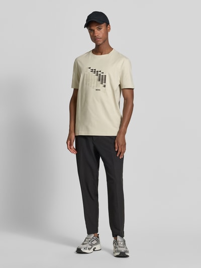 Männermodel trägt Relaxed Fit T-Shirt aus Baumwoll-Mix Modell 'TS_NETWORK FLAG' von BOSS Green in Beige mit Marken-Flag-Label, Ganzkörperansicht von vorne.