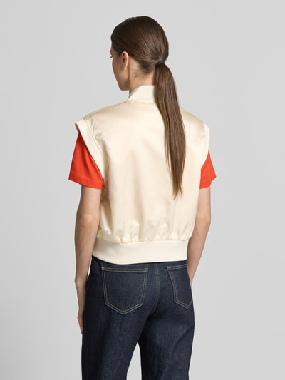 Frauenmodel trägt Weste mit Reißverschluss und Label-Detail von Original Bombers, creme mit roten Akzenten, lockerer Schnitt, Rückenansicht.