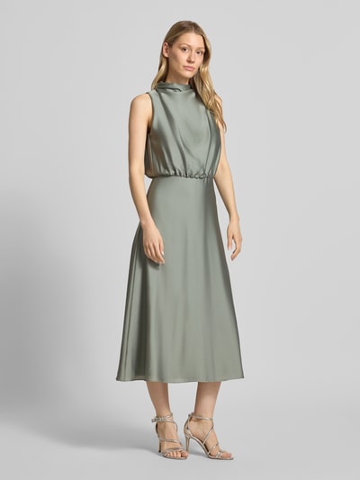 Frauenmodel trägt Cocktailkleid mit Stehkragen von Swing in sanftem Grün, Midikleid, glatte Textur, Ganzkörperansicht von vorne. Taillierte Passform, Reißverschluss hinten, Unterkleid, Rückenlänge 126 cm, Brustweite 34 cm.