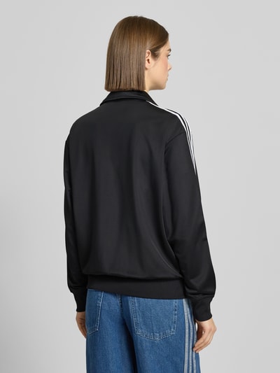 Frauenmodel trägt schwarze Sweatjacke mit Stehkragen von adidas Originals, Lockerer-Schnitt, Label-Stitching, Reißverschluss, Reißverschlusstaschen, gerippte Abschlüsse, Ganzkörperansicht Rückansicht.
