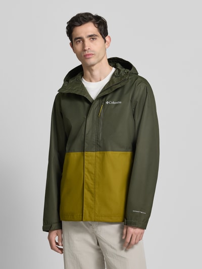 Männermodel trägt Jacke mit Kapuze Modell 'Hikebound™ II' von Columbia in Olivgrün und Gelb, Regular-Fit, verdeckter Reißverschluss, Logo, Ärmelriegel, Outdoor-Struktur, Ganzkörperansicht von vorne, Rückenlänge bei Größe M 74 cm, Schulterbreite 49 cm, Brustweite 61 cm, Ärmellänge 70 cm.