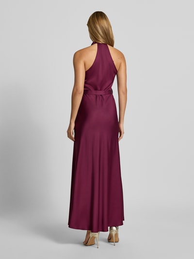 Frauenmodel trägt Abendkleid mit Neckholder von Rinascimento in Dunkelrot, glatte Textur, Stoffgürtel, Maxikleid, tailliert, Ganzkörperansicht Rückansicht.