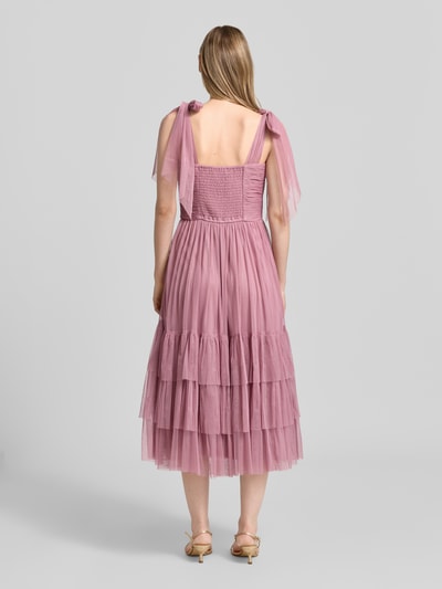 Frauenmodel trägt Knielanges Cocktailkleid im Stufen-Look von LACE & BEADS aus Mesh in A-Linie mit Drapierungen, Rückenlänge 104 cm, Ganzkörperansicht Rückansicht.