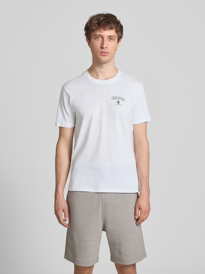 Männermodel trägt T-Shirt mit Logo und Rundhalsausschnitt von CHAMPION in Weiß, reine Baumwolle, Regular Fit, Ganzkörperansicht von vorne.