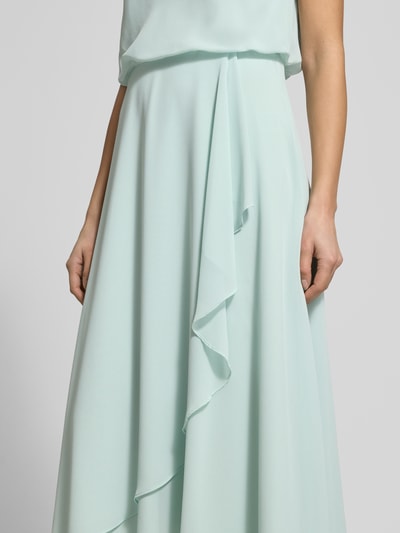 Kobieta modelka nosi 'Knielanges Cocktailkleid mit Wasserfall-Ausschnitt' od Christian Berg Cocktail z szyfonu, taliowany fason, długość do kolan, lejący dekolt, szerokie ramiączka, kopertowy styl dołu, zapięcie na haftkę i zamek błyskawiczny z tyłu, długość tyłu w rozmiarze 36: 120 cm, szerokość klatki piersiowej w rozmiarze 36: 45 cm, widoczne gładkie jasnomiętowe kolory i delikatna tekstura, detalowe ujęcie środkowej części sukienki.
