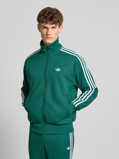 Męski model nosi Trainingsjacke mit Stehkragen od adidas Originals w kolorze zielonym, krój regular fit, widok całej sylwetki z przodu