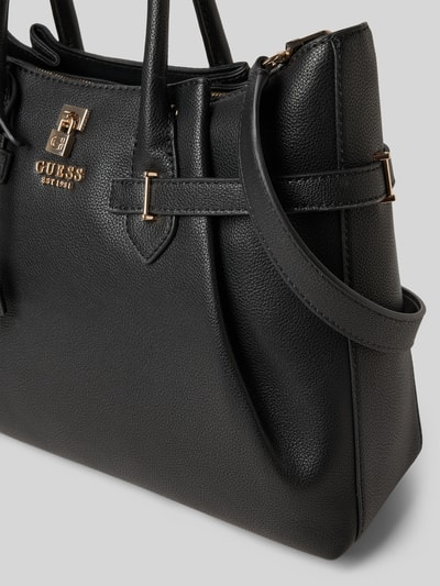 Produktfoto, czarna Handtasche in Leder-Optik mit Logo-Applikation od Guess, złote detale, faktura skóropodobna, zbliżenie na detal, główna komora na zamek, odpinany pasek, uchwyty, wymiary 40x25x13 cm, długość paska 115 cm.