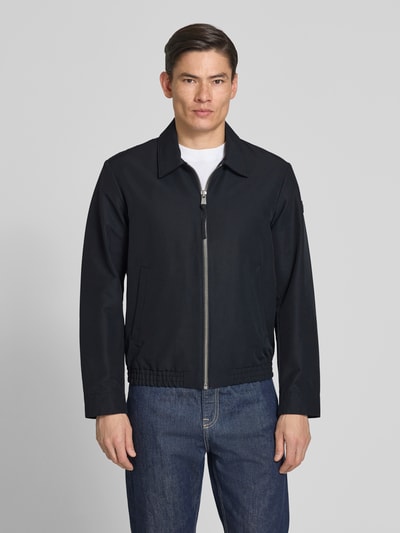 Männermodel trägt Regular Fit Blouson mit elastischem bund van Marc O'Polo, look: effen, regular fit pasvorm, platte kraag, ritssluiting, labelpatch, lange mouw met drukknoop, rompzoom elastisch, zij-steekzakken, binnenzak. Ganzkörperansicht von vorne.