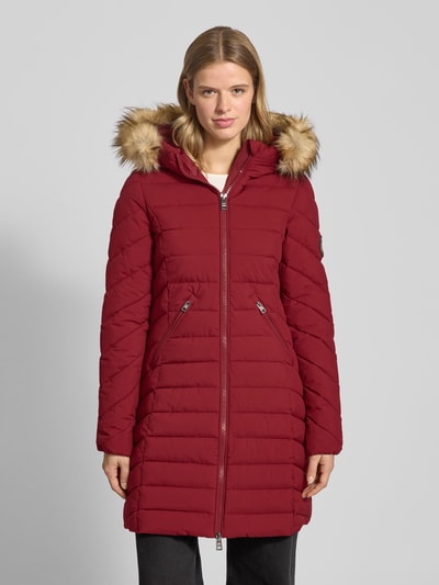 Vrouwenmodel draagt Regular Fit Steppmantel met Kunstfellbesatz Modell 'Fuji' van Superdry in bordeauxrood met ritszakken, logo-patch, geheel lijf vooraanzicht.