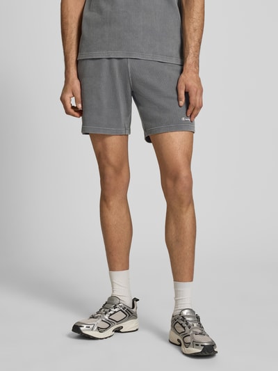 Mężczyzna nosi Shorts mit Strukturmuster und elastischem Bund od CHAMPION, bawełniany miks, krój regular fit, szare, Szerokość w rozmiarze M 40 cm, długość nogawki 19 cm, przód, zbliżenie na dolną połowę ciała