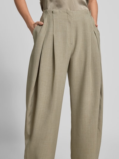 Frauenmodel trägt Wide Fit Stoffhose mit Bundfalten von Iro in Beige, mit Eingrifftaschen, Haken- und Reißverschluss, Nahaufnahme Oberkörper.