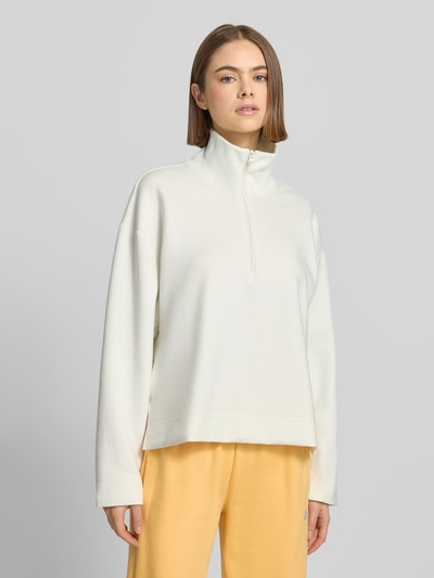 Modelka kobieca nosi Pullover mit Stehkragen und Reißverschluss od adidas Sportswear, kremowy poliesterowy miks, logo, relaxed fit, zamek, pełny widok z przodu.