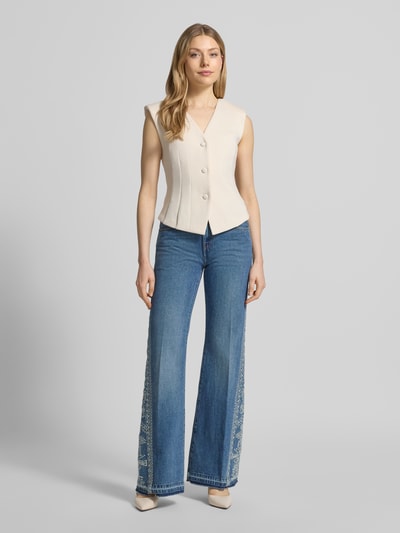 Frauenmodel trägt Flared Jeans mit Motiv-Stitching Modell 'VIVY' von Bash, Reine Baumwolle, ausgestellter Schnitt, 5-Pocket-Design, Knopf- und Reißverschluss, mittleres Blau mit hellem Muster, Ganzkörperansicht von vorne.