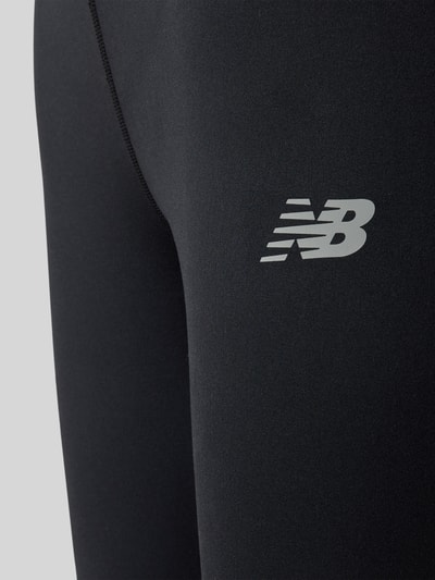 Frauenmodel trägt Slim Fit Leggings mit Logo-Print Modell 'Harmony' von New Balance, schwarze Jersey-Textur, Nahaufnahme Oberschenkel.
