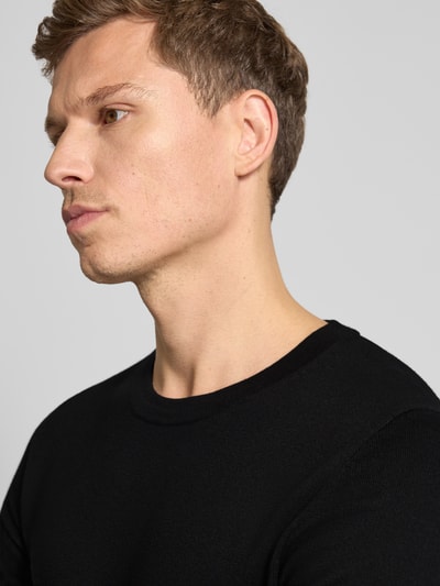 Męski model nosi czarny Sweter z dzianiny z bawełny, krój regular fit od Drykorn, model 'Irmino', prążkowane wykończenia, okrągły dekolt, zbliżenie na górną część ciała.