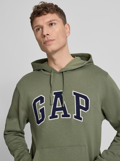 Männermodel trägt Hoodie mit Kängurutasche von GAP aus Baumwoll-Mix, lockere Passform, Label-Stitching, Nahaufnahme Oberkörper.