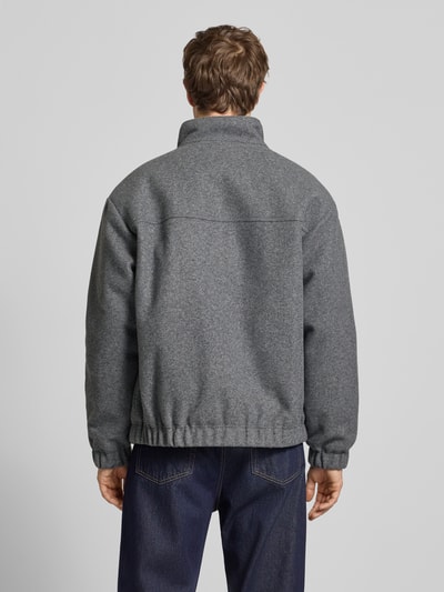 Męskimodel nosi Regular Fit Bomberka z dodatkiem wełny od Tommy Jeans, melanż, stójka, zamek błyskawiczny, wpuszczane kieszenie, długi rękaw, elastyczne zakończenia, haftowane logo; widok całej sylwetki z tyłu.