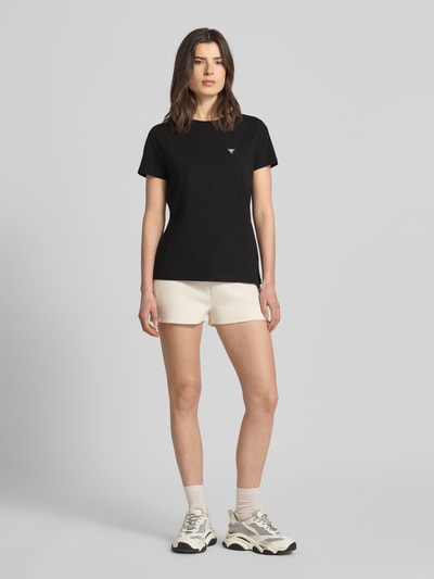 Kobiece modelka nosi Regular Fit T-Shirt mit Logo-Applikation Modell 'Colette' od Guess Activewear, czarny t-shirt z okrągłym dekoltem, elastyczna bawełniana mieszanka, długość pleców w rozmiarze S: 60 cm, Ganzkörperansicht von vorne.