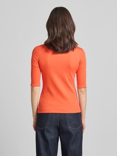 Frauenmodel trägt T-Shirt mit Label-Applikation von Marc Cain in Orange, körpernaher Schnitt, U-Ausschnitt, mitteldicke Baumwoll-Mix-Textur, Ganzkörperansicht Rückansicht.