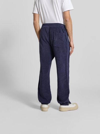 Männermodel trägt Sweatpants aus reiner Baumwolle von RHUDE in Dunkelblau, lockere Passform, Frottee, elastischer Bund, Ganzkörperansicht Rückansicht.