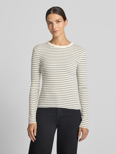 Frauenmodel trägt Slim Fit Longsleeve aus reiner Baumwolle Modell 'NURIT' von DRYKORN, feine schwarze Streifen auf cremefarbenem Stoff, Rundhalsausschnitt, dezente Struktur, Rückenlänge S 57 cm, Ganzkörperansicht von vorne.