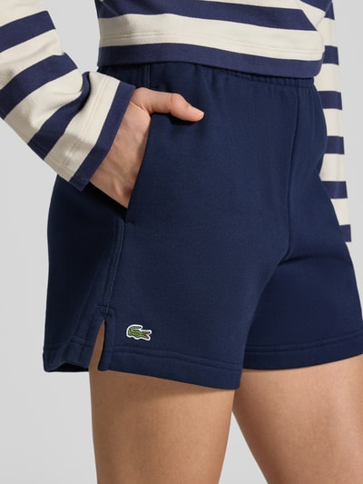 Kobiece model prezentuje Regular Fit Sweatshorts aus reiner Baumwolle od Lacoste, efekt: jednolity kolor, krój regular fit, wyhaftowane logo, tunel, ściągacz: elastyczny, wpuszczane kieszenie, materiał: bawełna, zbliżenie na biodra