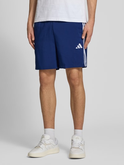 Männermodel trägt Regular Fit Sport-Shorts mit elastischem Bund von adidas Sportswear, unifarben blau, Kontraststreifen, Nahaufnahme Oberschenkel.