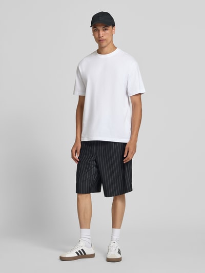 Męski model nosi szorty z elastycznym pasem model 'CRISTIANO' od Redefined Rebel, mieszanka materiałów z dodatkiem streczu, krój relaxed fit, szerokość w rozmiarze M: 42 cm, długość wewnętrzna nogawki: 27 cm, ciemne kolory z białymi paskami, gładka faktura, całopostaciowy widok z przodu.