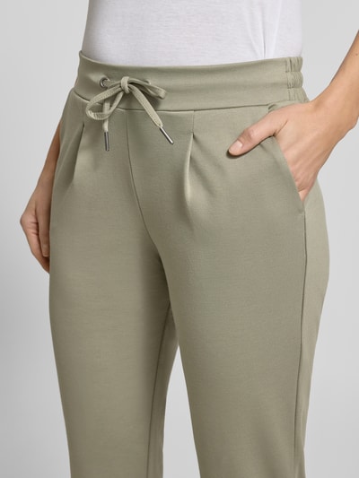 Frauenmodel trägt Slim Fit Stoffhose mit Viskose-Anteil Modell 'Rizet' von B.Young in hellem Khaki, mit elastischem Bund, Bundfalten, 7/8-Länge, Nahaufnahme Hüftbereich. Elastischer Material-Mix, Bundweite 37 cm, Innenbeinlänge 68 cm.