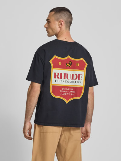 Männermodel trägt Relaxed Fit T-Shirt mit Logo-Print von RHUDE aus reiner Baumwolle, schwarzer Stoff, große rote und gelbe Grafik, Rückenlänge 67 cm, Ganzkörperansicht Rückansicht.
