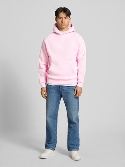 Männermodel trägt Hoodie mit Känguru-Tasche von REVIEW in Rosa aus Baumwollmischung, lockere Passform, Ganzkörperansicht von vorne.