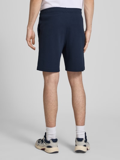 Männermodel trägt Shorts mit Label-Stitching mit elastischem Bund von CHAMPION in Dunkelblau, Regular Fit, Baumwoll-Mix, Ganzkörperansicht Rückansicht.