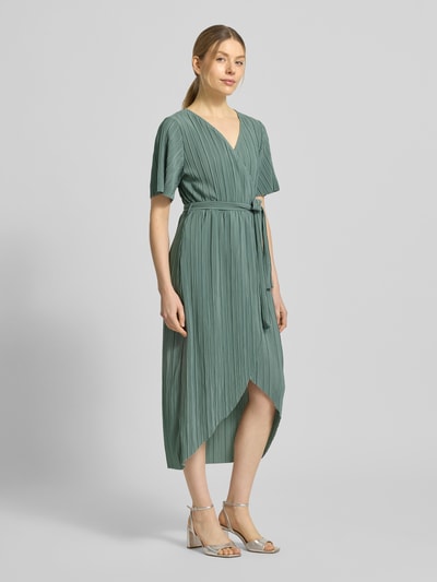Frauenmodel trägt Cocktailkleid in Wickel-Optik Modell 'LINDA' von YAS in Grün mit V-Ausschnitt, Bindegürtel, Midilänge, Ganzkörperansicht von vorne.