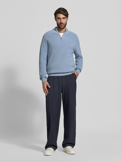 Męski model nosi Regular Fit Strickpullover aus reiner Baumwolle mit Troyer-Kragen od Fynch-Hatton, jasnoniebieski, prążkowane wykończenia, haftowane logo, dzianinowa faktura, długi rękaw, długość pleców w rozmiarze M: 65 cm, długość rękawa w rozmiarze M: 75 cm, widok całej sylwetki z przodu.