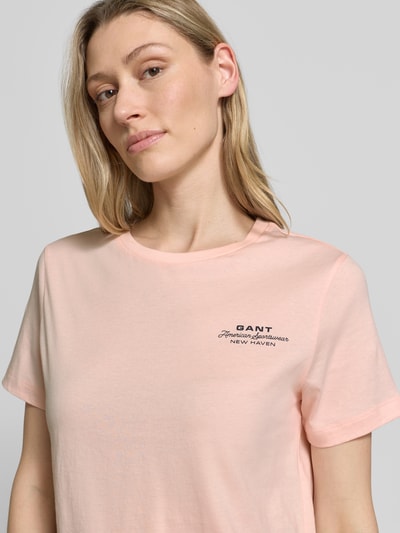 Modelka nosi T-Shirt mit Label-Print und Rundhalsausschnitt von Gant z bawełny, krój regular fit, jasnoróżowy, nadruk z logo, długość tyłu 57 cm, rozmiar S, zbliżenie na górę ciała