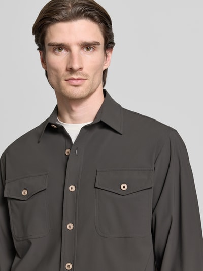 Männermodel trägt Hemdjacke mit Knopfleiste von CRUNA in Dunkelgrau, Material-Mix mit Stretch, Brusttaschen, Nahaufnahme Oberkörper.