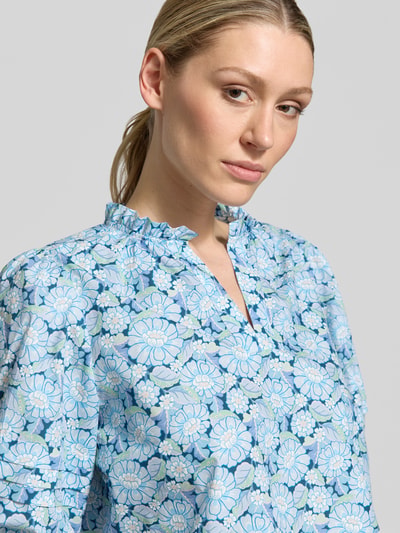 Frauenmodel trägt Bluse mit Serafino-Kragen und Ballonärmeln von Rich & Royal aus Reine Baumwolle, florales Muster in Blau und Weiß, Nahaufnahme Oberkörper.
