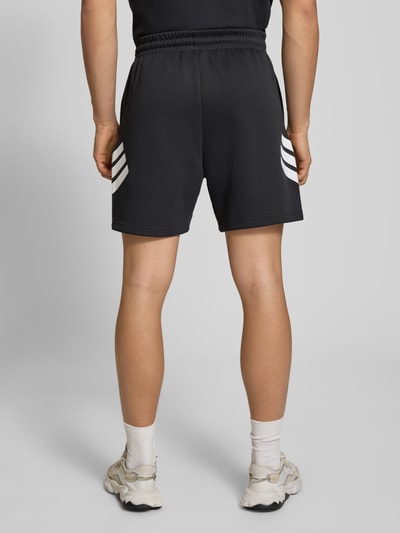 Männermodel trägt Regular Fit Sport-Shorts mit Logo-Print von adidas Sportswear, unifarben, elastischer Bund, seitliche Taschen, Ganzkörperansicht Rückansicht.